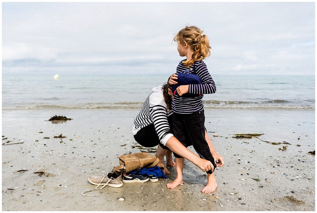 maman qui aide sa fille à retrousser son pantalon sur la plage