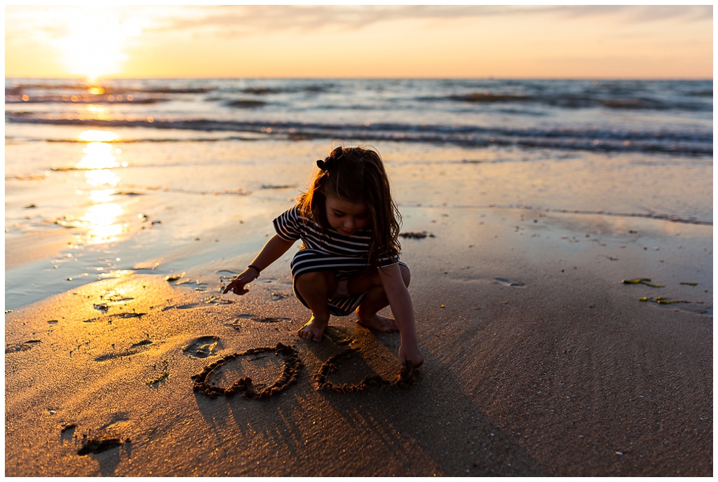 petite fille qui dessine un coeur dans le sable à la golden hour. Audrey GUYON, photographe famille normandie