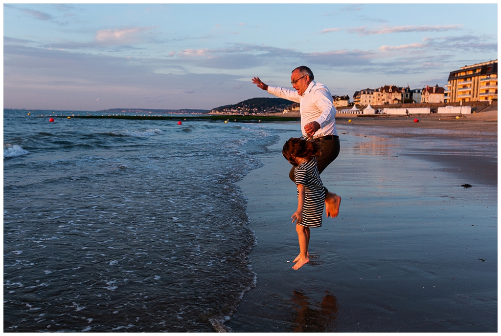 papa et sa fille qui sautent au bord des vagues à cabourg. photographe famille cabourg, audrey guyon