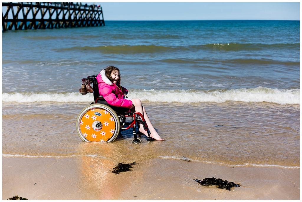 jeune fille les pieds dans l'eau avec son fauteuil roulant